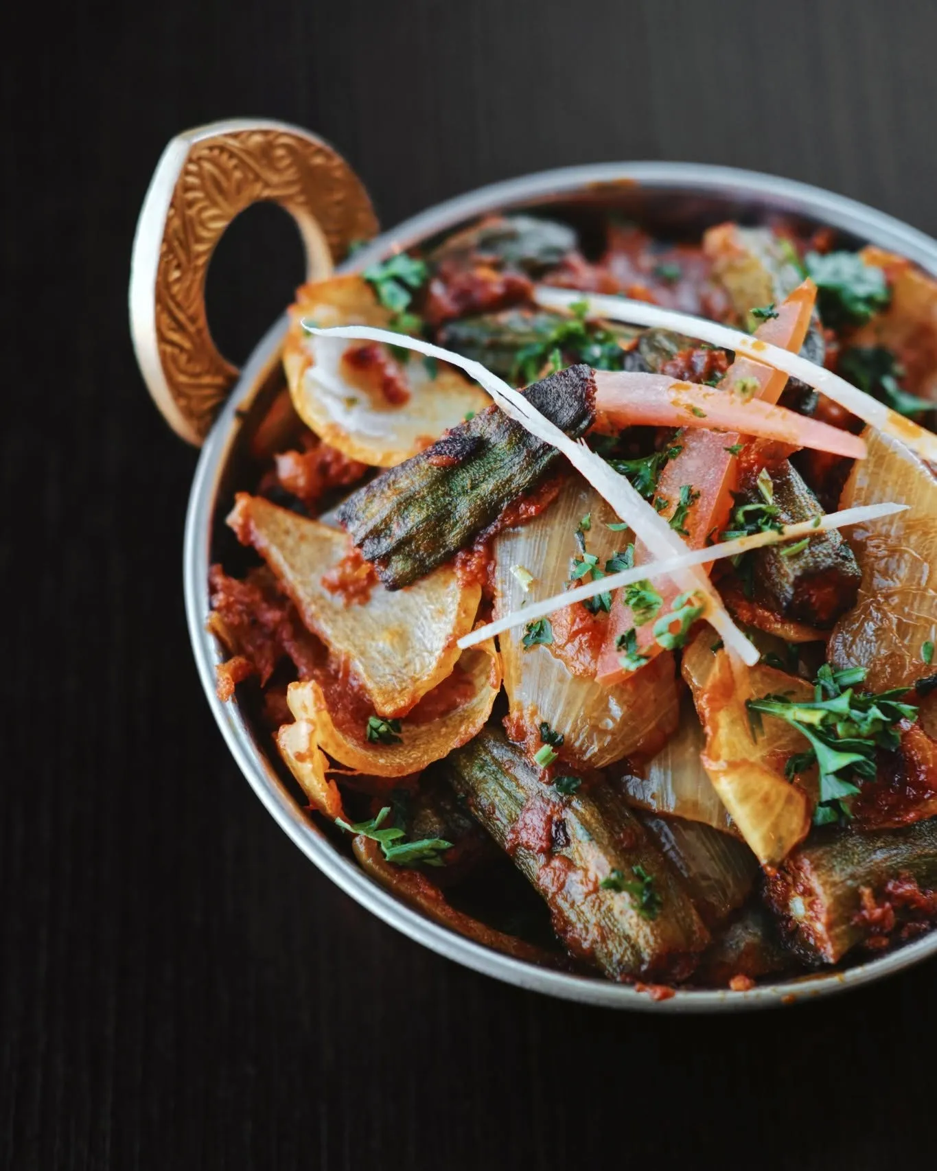 Spiced okra in a karahi on dark wood